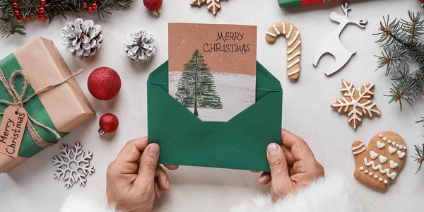 サンタクロースはテーブルでメリークリスマスのための挨拶と封筒を保持 — ストック写真