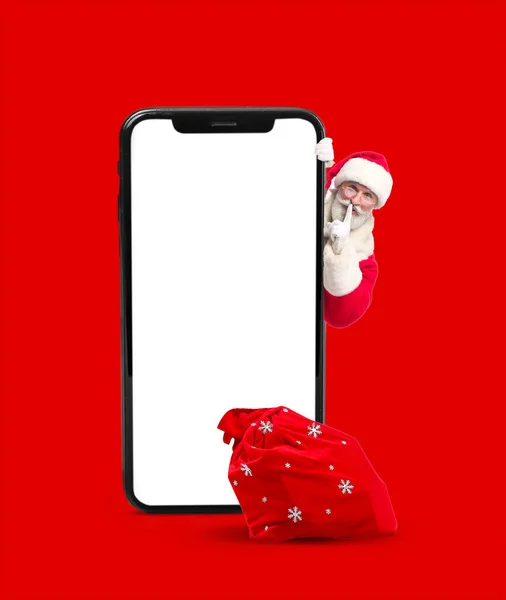 Санта Клаус Большим Смартфоном Сумкой Показывающей Жест Молчания Красном Фоне — стоковое фото