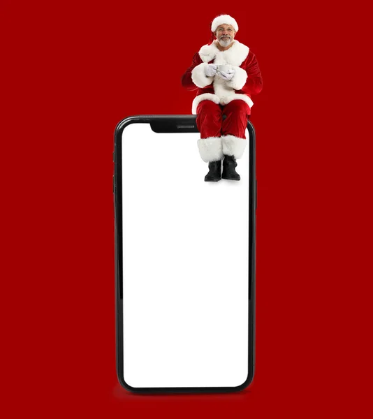 Der Weihnachtsmann Sitzt Auf Einem Großen Smartphone Und Trinkt Heiße — Stockfoto