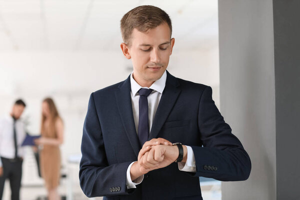 Young bank manager looking at wristwatch in office