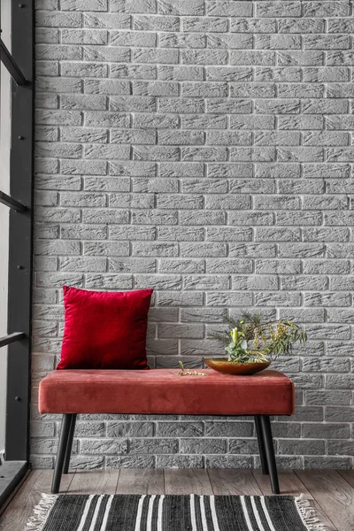 灰色のレンガの壁の近くの柔らかいベンチで美しいいけばなとクッション — ストック写真