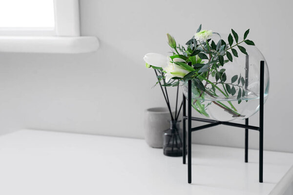Beautiful ikebana, candle and reed diffuser on table near light wall