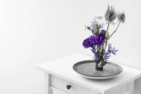 stock image Bowl with beautiful ikebana on table near light wall