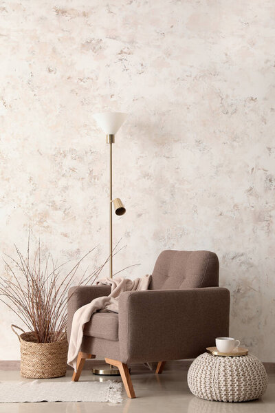 Stylish armchair, floor lamp and decor near light wall