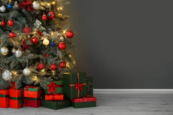 輝く光と暗い壁の近くにプレゼントクリスマスツリー — ストック写真