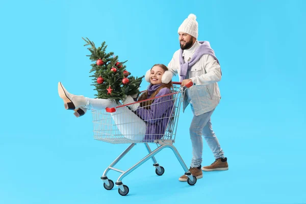Junges Paar Mit Weihnachtsbaum Und Einkaufswagen Auf Blauem Hintergrund — Stockfoto