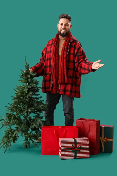 緑の背景にクリスマスツリー ショッピングバッグや贈り物を持つハンサムな男 — ストック写真