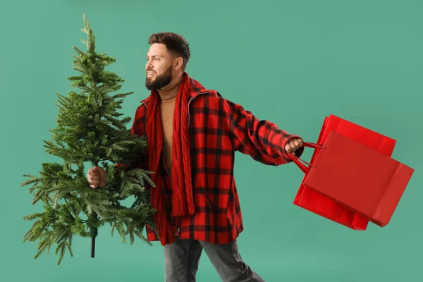 Schöner Mann Mit Weihnachtsbaum Und Einkaufstüten Auf Grünem Hintergrund — Stockfoto