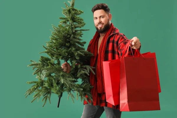 緑の背景にクリスマスツリーとショッピングバッグを持つハンサムな男 — ストック写真