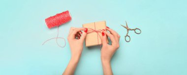 Mavi arka planda Noel hediyesi kutusunu bağlayan kadın elleri