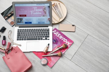 Diz üstü bilgisayar, açık bir sayfa dolusu güzellik blogu, dergi, dekoratif kozmetik ürünler ve açık ahşap zeminde aksesuarlar.