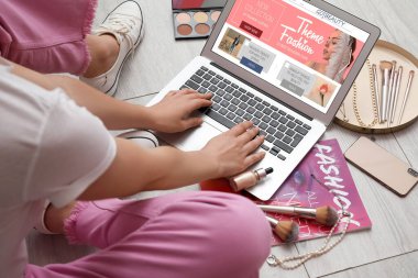 Dizüstü bilgisayarı, dekoratif kozmetik ürünleri ve hafif ahşap zeminde aksesuarları olan kadın güzellik blogcusu.