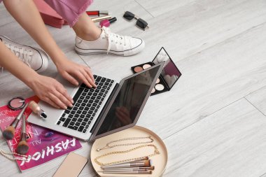 Dizüstü bilgisayarı, dekoratif kozmetik ürünleri ve hafif ahşap zeminde aksesuarları olan kadın güzellik blogcusu.