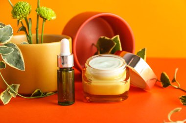 Krema kavanozu, kozmetik şişesi ve kırmızı arka planda güzel bir ikebana.