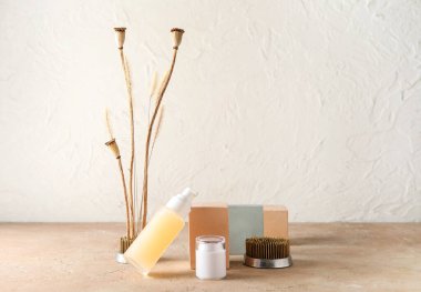 Beyaz duvarın yanındaki masada ikebana ve dekor içeren kozmetik ürünleri.