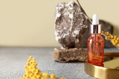 Kozmetik şişesi, çiçekler ve taşlar renk duvarının yanındaki masada, yakın plan.