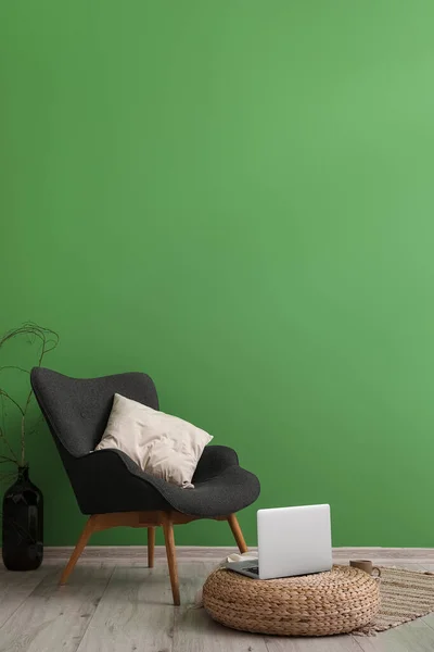 stock image Stylish armchair with pillow and modern laptop near color wall