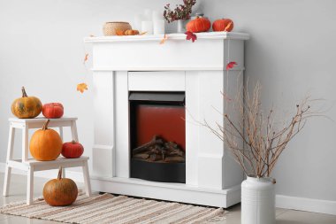 Ağaç dalları, merdiven, Cadılar Bayramı balkabakları ve ışık duvarı yakınında şömine olan vazolar.