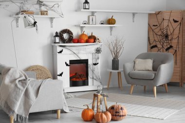 Cadılar Bayramı için dekore edilmiş aydınlık oturma odasının içinde şömine, kanepe ve koltuk var.