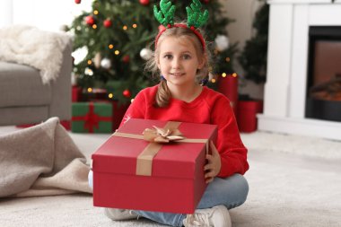 Evde Noel hediyesiyle ren geyiği boynuzları içinde mutlu küçük kız.