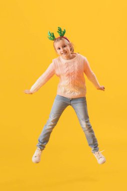 Geyik boynuzlarıyla mutlu küçük kız sarı arka planda zıplıyor