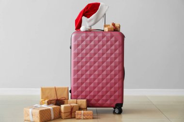 Noel Baba şapkalı bavul ve gri duvarın yanında Noel hediyeleri