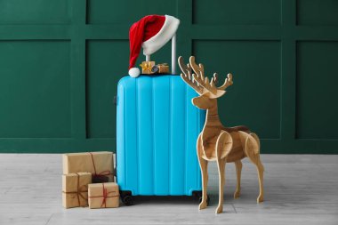 Noel Baba şapkalı bavul, Noel hediyeleri ve yeşil duvarın yanında tahta ren geyiği.