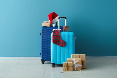 Noel Baba şapkalı bavullar, pasaportlar ve mavi duvarın yanındaki Noel hediyeleri.