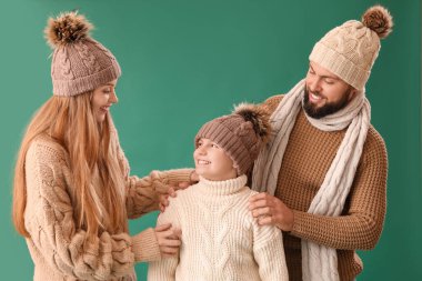 Küçük oğulları yeşil arka planda sıcak giysiler içinde mutlu bir aile.