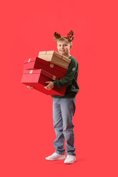 ハッピー小さな男の子でトナカイ角でクリスマスプレゼント上の赤い背景 — ストック写真