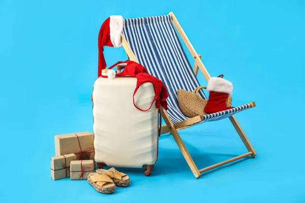 Noel Baba şapkalı bavul, Noel hediyeleri, seyahat aksesuarları ve mavi arka planda iskemle.