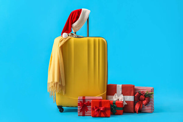 Suitcase with Santa hat and Christmas gifts on blue background