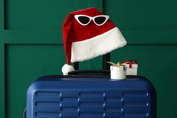 Koffer Met Kerstmuts Zonnebril Kerstcadeaus Bij Groene Muur — Stockfoto