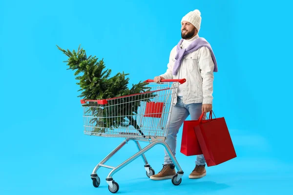 青い背景にショッピングカート バッグ クリスマスツリーを持つハンサムな男 — ストック写真
