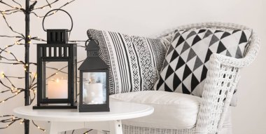 Masada yanan mumlar, odada hasır koltuklar olan siyah Noel fenerleri.