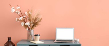Çiçekli vazo ve masadaki pembe duvarın yanında boş ekranlı dizüstü bilgisayar.