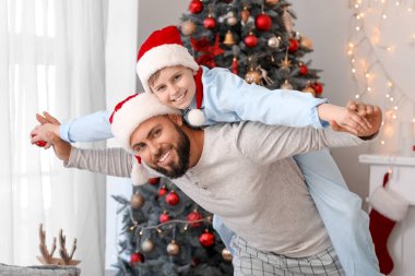 Mutlu baba ve Noel Baba şapkalı küçük oğlu Noel arifesinde evde eğleniyorlar.