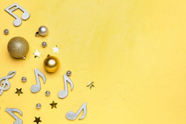 Sarı zemin üzerinde notalar ve Noel topları olan kompozisyon