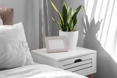 Bedside table with photo frame and houseplant in light bedroom clipart