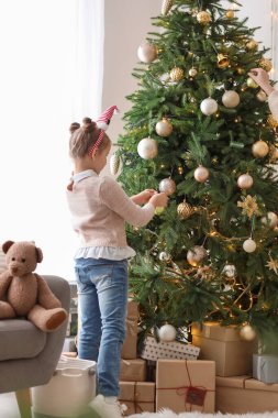 Noel Baba şapkalı küçük kız evde Noel ağacı süslüyor.
