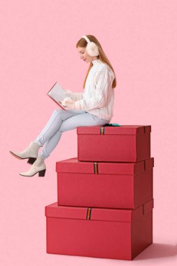 Noel hediyeli genç bir kadın pembe arka plan üzerine kitap okuyor.