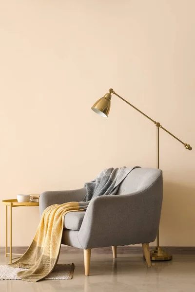 stock image Stylish armchair with plaid and floor lamp near color wall