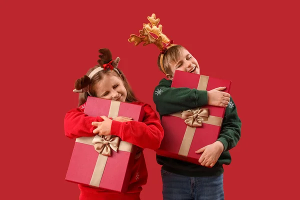 Kleine Kinder Rentierhörnern Umarmen Weihnachtsgeschenke Auf Rotem Hintergrund — Stockfoto