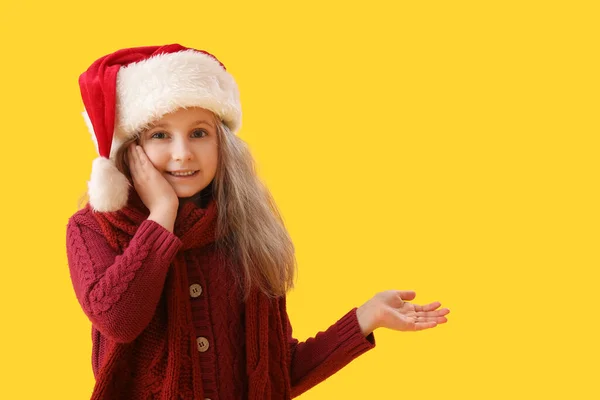 Маленька Дівчинка Санта Капелюха Показує Щось Жовтому Тлі — стокове фото