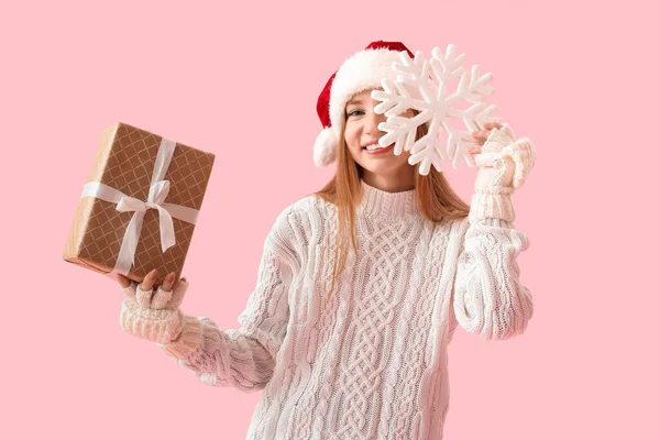 若いです女性でサンタ帽子とともにクリスマスプレゼントや雪の結晶上のピンクの背景 — ストック写真
