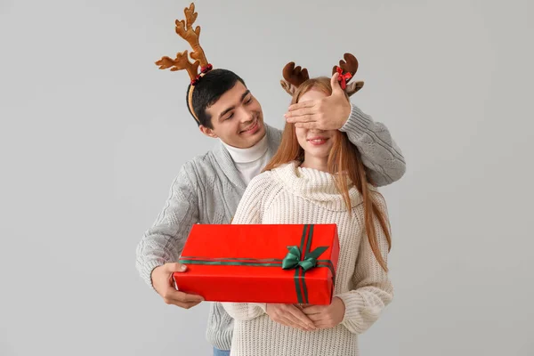 Jovem Surpreendendo Sua Namorada Com Presente Natal Fundo Cinza — Fotografia de Stock