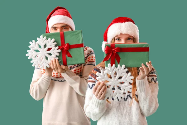 Счастливая Молодая Пара Шляпах Санты Рождественскими Подарками Снежинками Зеленом Фоне — стоковое фото