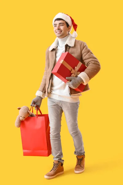 头戴圣诞礼帽 头戴黄色背景购物袋的年轻人 — 图库照片