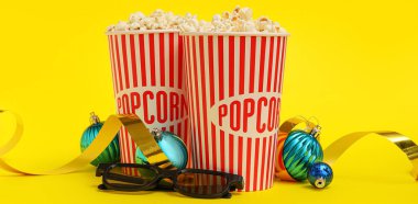 3 boyutlu gözlüklü patlamış mısır ve sarı arka planda Noel topları.