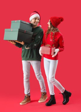 Kırmızı arka planda Noel hediyelerine aşık genç çift